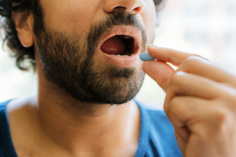 A medium-skinned man is taking a blue PrEP pill