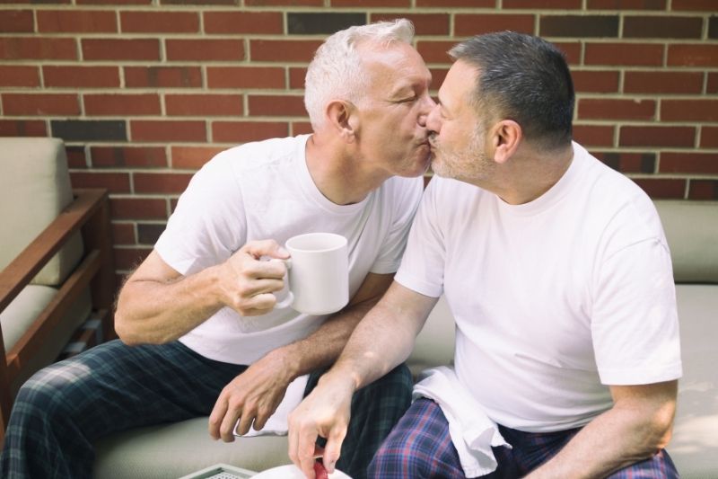 Two older light-skinned men kissing.