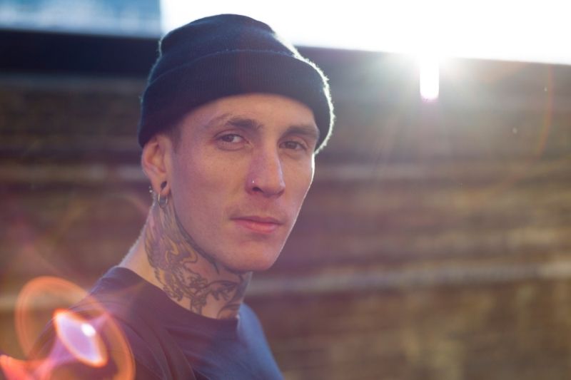 A light-skinned man with tattoos and a knit cap looking at the camera.