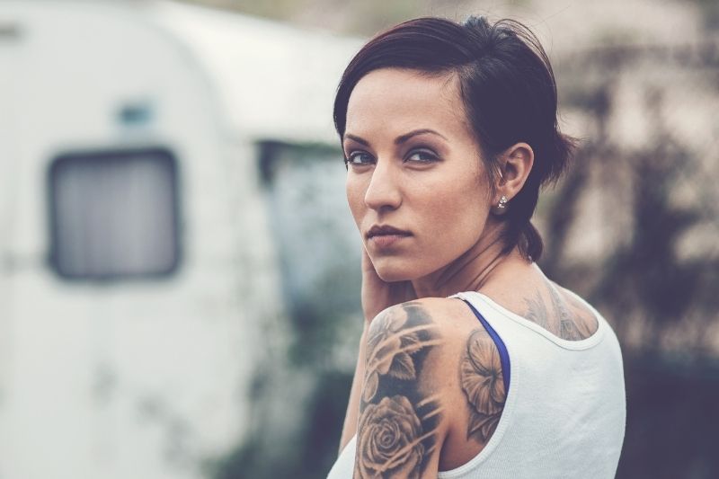 A light-skinned woman with tattoos looking over her left shoulder at the camera.