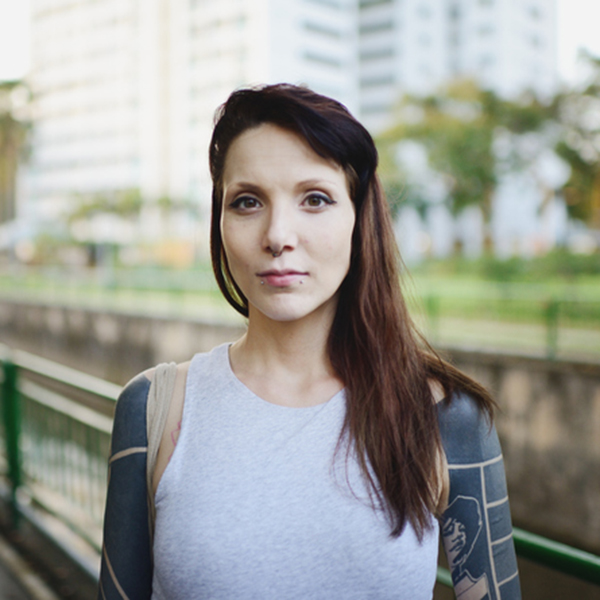 A light-skinned woman with tattoos staring at the camera in a park.