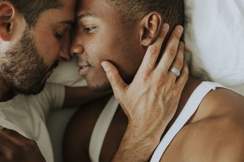 Two men in bed holding each other tenderly.