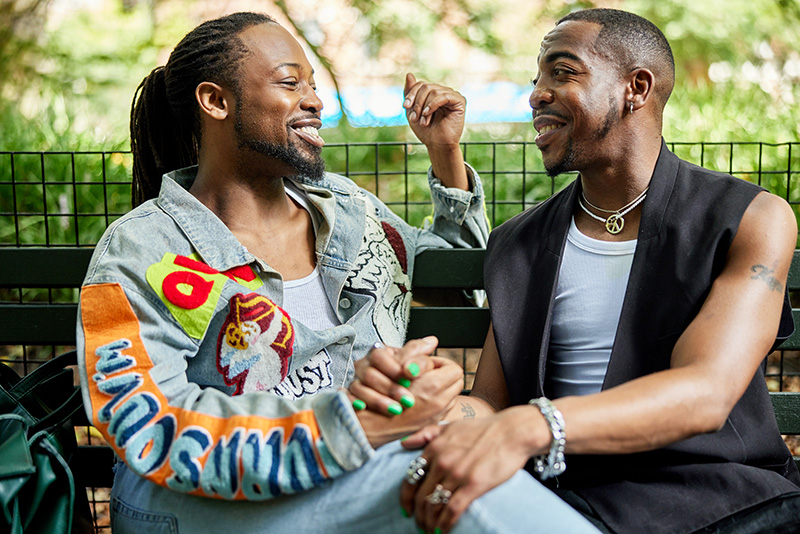 Two darker-skinned men in conversation sit next to each other on a park bench