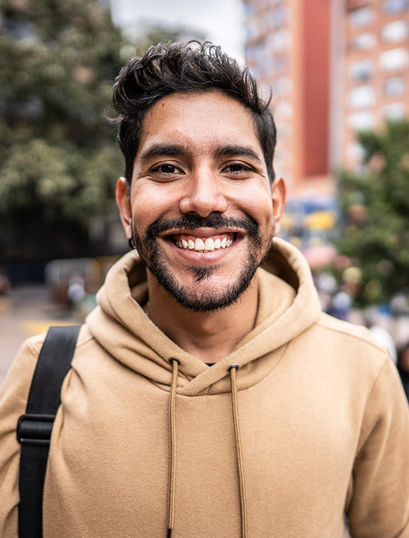 A medium skinned man with dark hair and beard smiles at the camera