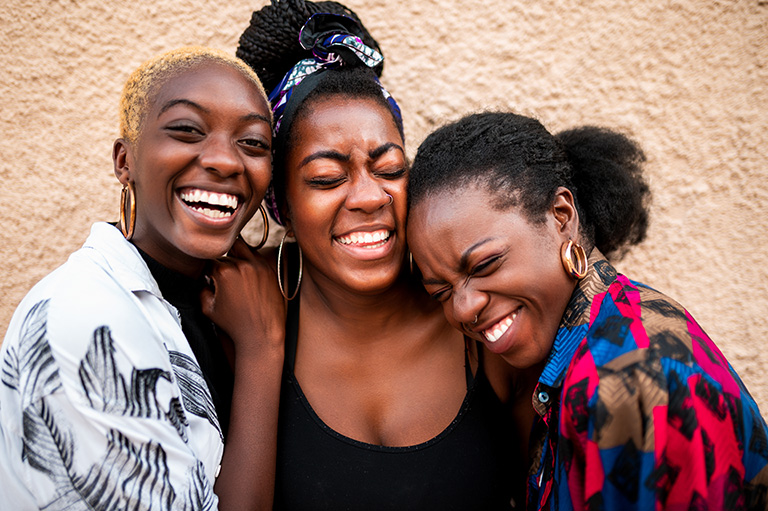 A group of darker skinned women embrace and laugh together