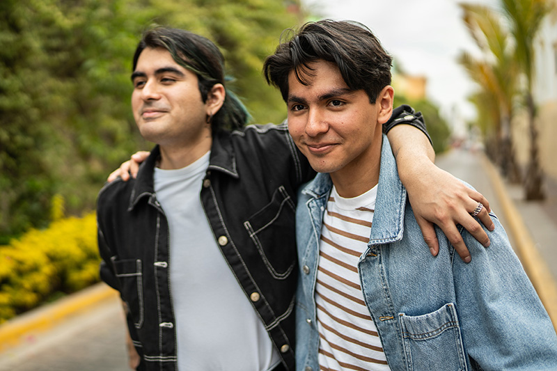 Two medium-skinned men embrace while walking down the street