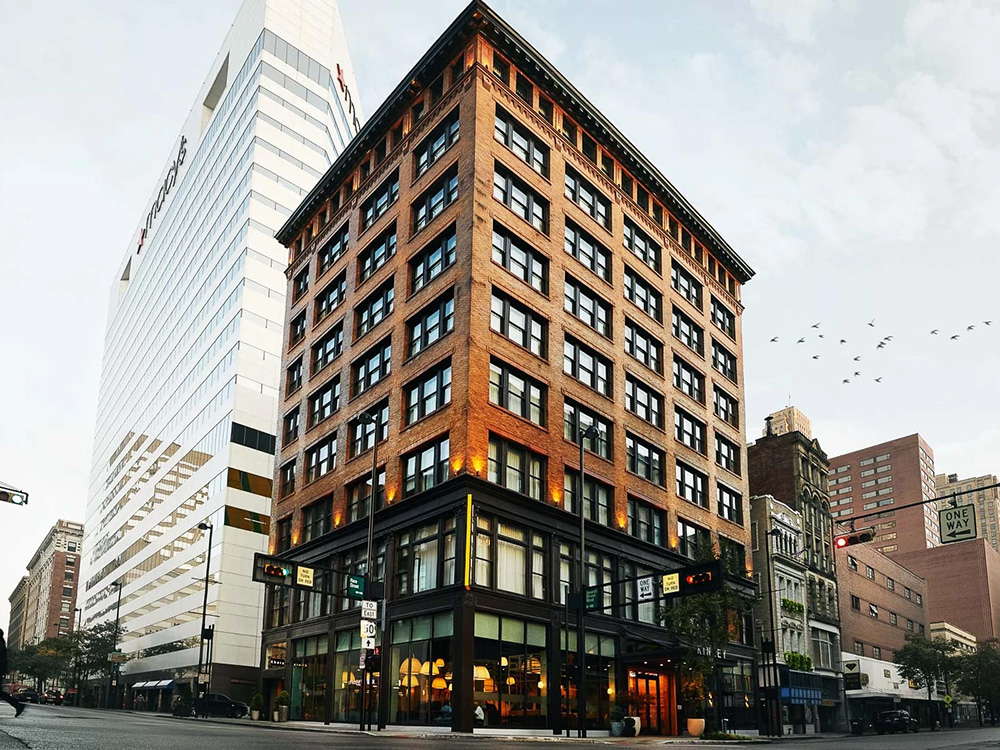 Exterior of the Kinley Hotel Cincinnati, a refurbished brick building with large windows, a black awning over the entrance, and “Kinley” in bold white letters above the door.
