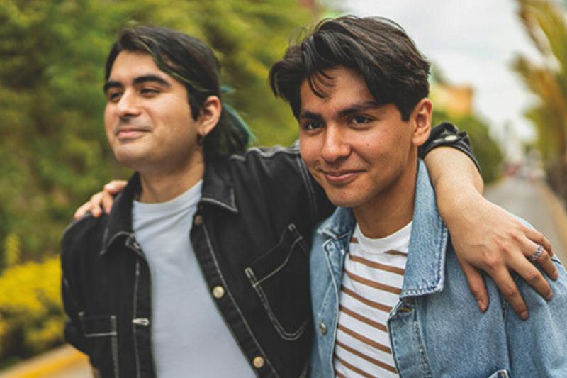 Two Latino men with their arms draped over each others shoulders
